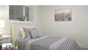 Een slaapkamer met een bed, een nachtkastje, een raam met jaloezieën en een stadsgezicht op de muur.