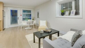 Een moderne woonkamer met een grijze bank, een salontafel en een eethoek met een witte tafel en stoelen.