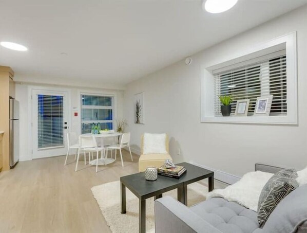 Un salon moderne avec un canapé gris, une table basse et un coin repas comprenant une table et des chaises blanches.