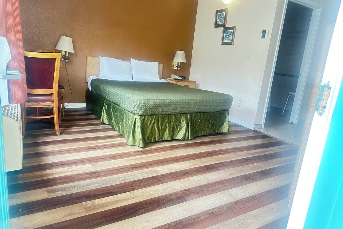 A hotel room with a bed, a chair, a nightstand, and a door.