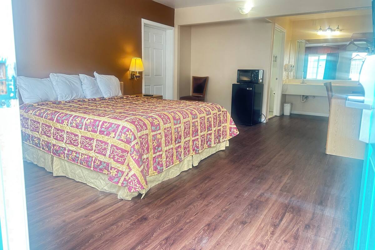 A hotel room with a large bed, a desk, a chair, a microwave, and a small refrigerator.