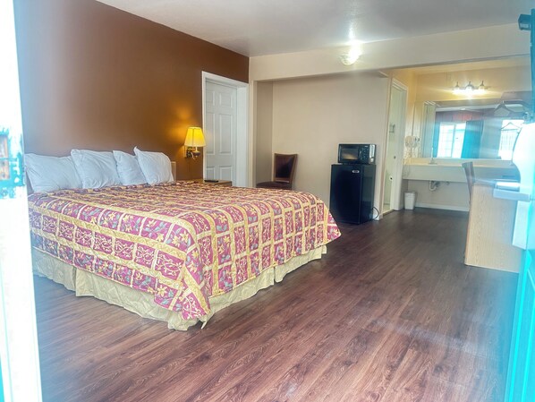 Una habitación de hotel con una cama grande, un escritorio, una silla, un microondas y un refrigerador pequeño.
