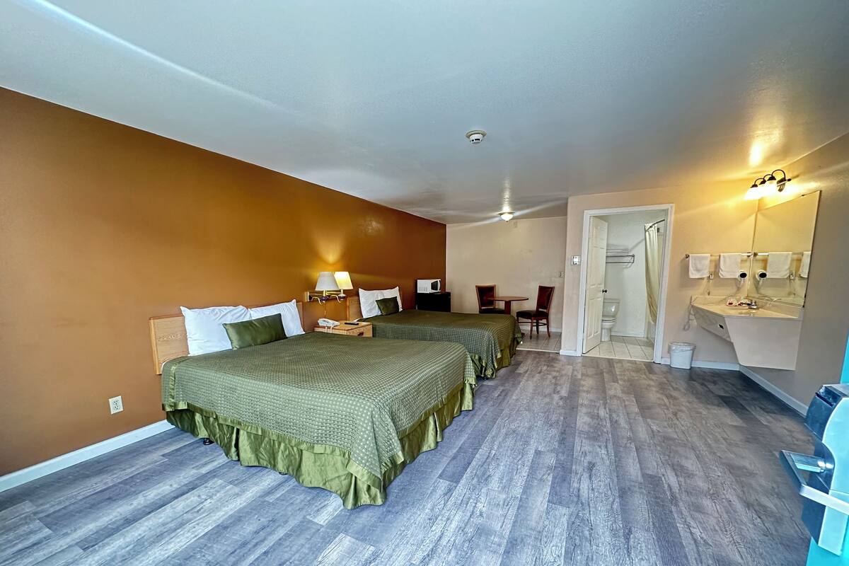 A hotel room with two beds, a bathroom, and a small seating area.