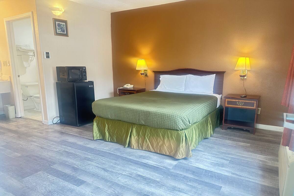 A hotel room with a bed, two bedside lamps, a TV, and a small desk.