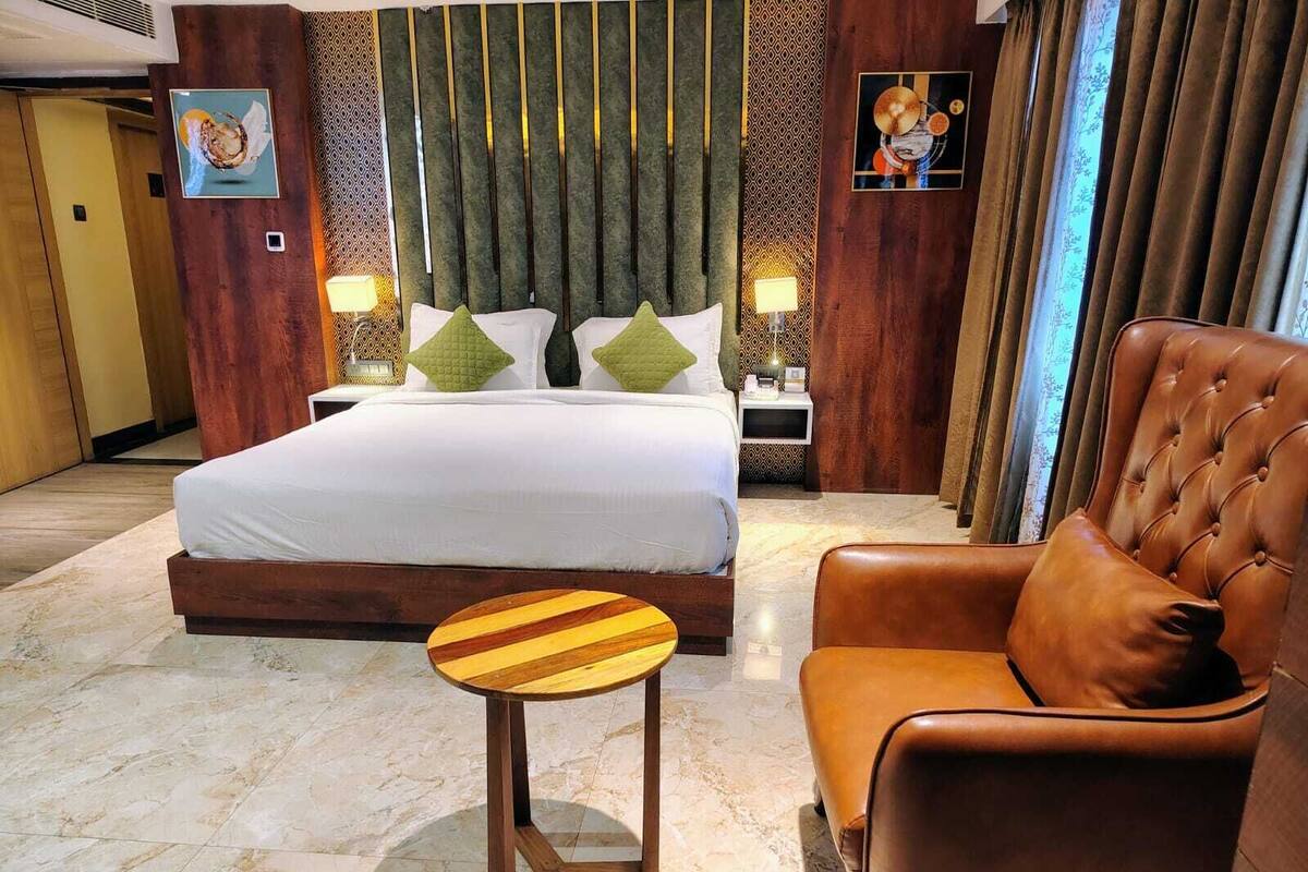 A hotel room with a bed, a leather armchair, a small wooden table, and a nightstand with lamps.