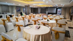 Un salón de banquetes con mesas y sillas redondas, cada una con manteles blancos y fajas doradas.