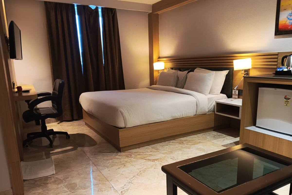 A hotel room with a bed, a desk, a chair, a TV, a lamp, a refrigerator, and a window with curtains.