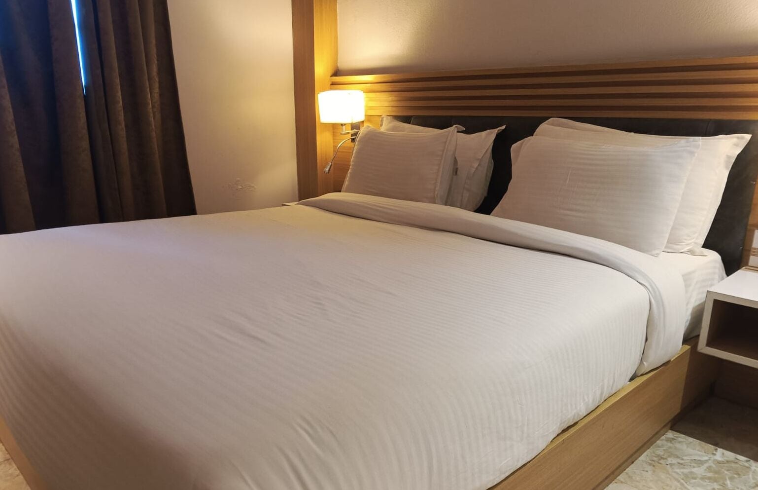 Een hotelkamer met een groot bed, een houten hoofdbord, een nachtkastje en een bedtafel.
