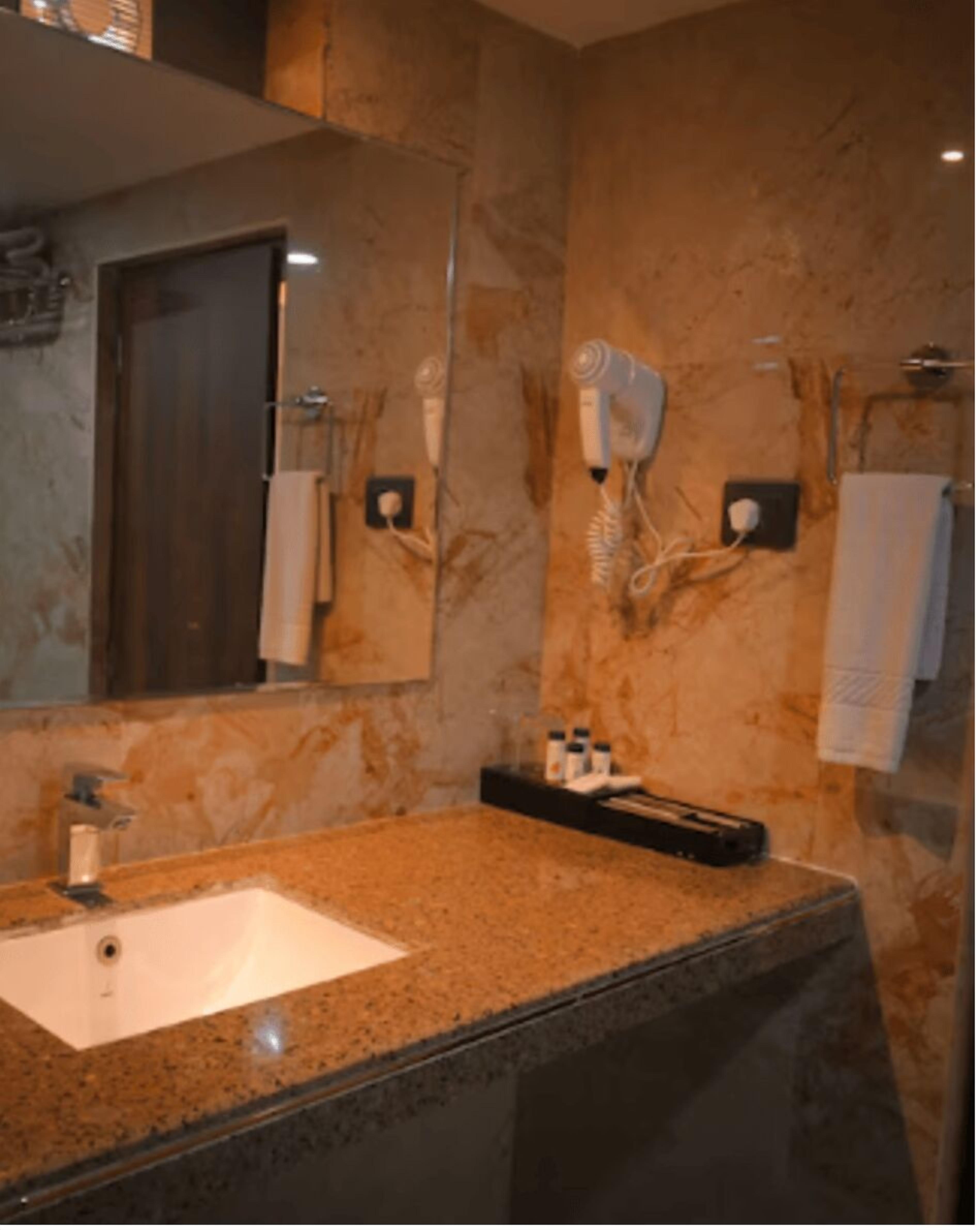 A bathroom with a granite countertop, a sink, a mirror, a hairdryer, and a towel rack.