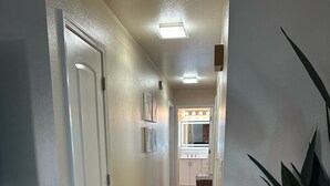 A hallway with wooden flooring, white walls, and a door on the left.