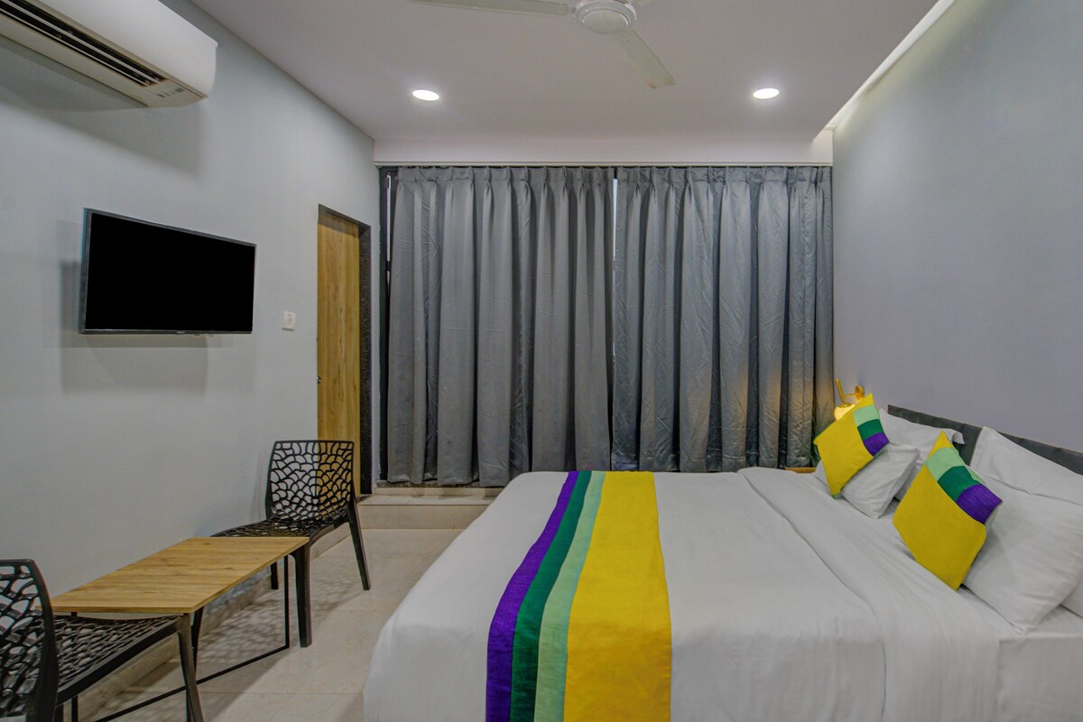 A hotel room with a bed, a TV mounted on the wall, a chair, and a desk.