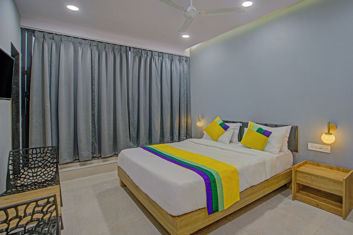 A bedroom with a bed, curtains, a nightstand, and a wall-mounted light.