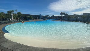 Une grande piscine extérieure à l’eau d’un bleu limpide, entourée de chaises longues et de palmiers.