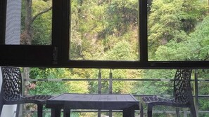 A room with a view of dense foliage through a window. There is a table and two chairs in the foreground. - Kempty Lake Adventure Resort (Dhanaulti)