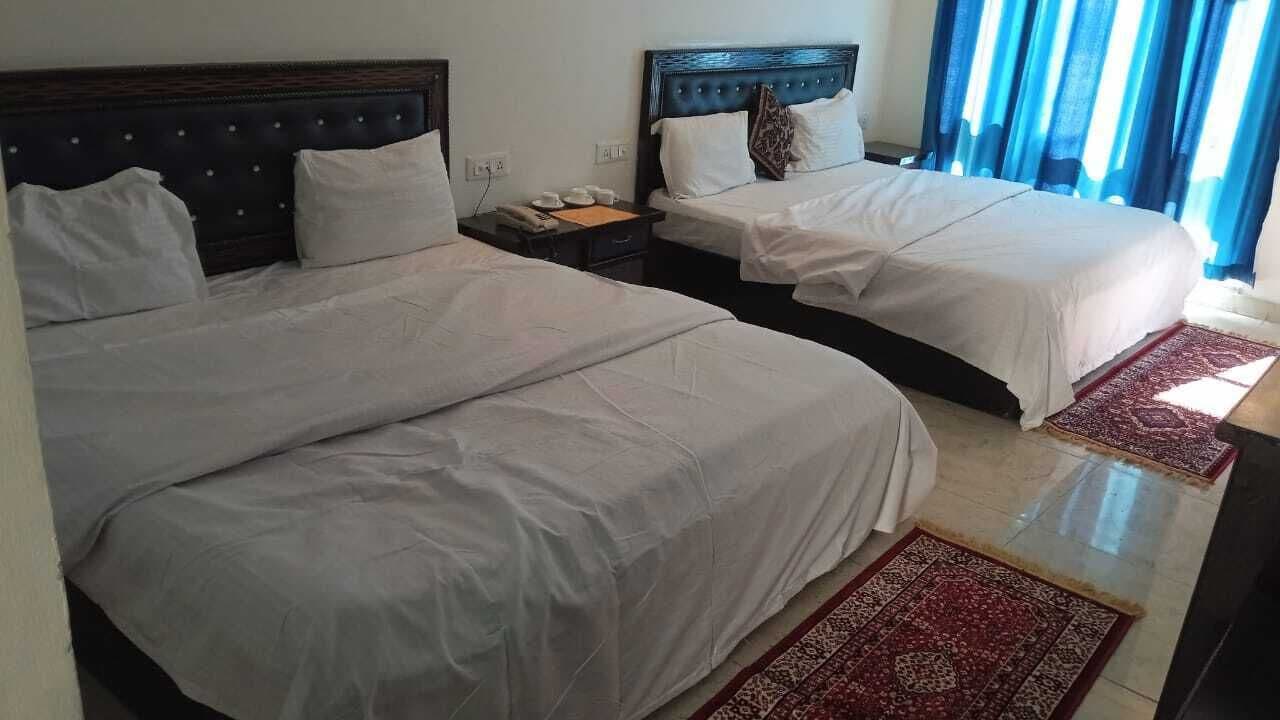 A hotel room with two beds, a nightstand, and a window with curtains.