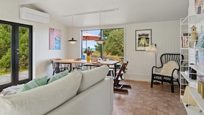 A room with a white sofa, dining table, chairs, and a bookshelf.