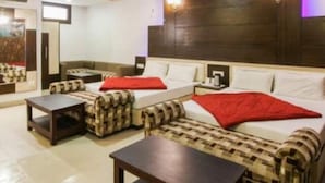A hotel room with a sofa set, a bed, a small table, and a ceiling fan. - Hotel Eminent (Agra)