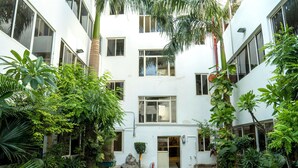 A white multi-story building with a central entrance, surrounded by lush greenery and a small lawn. - Hotel Eminent (Agra)