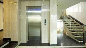 An interior view of a hotel lobby with a marble floor, a glass elevator, and a staircase with metal railings. - Hotel Eminent (Agra)