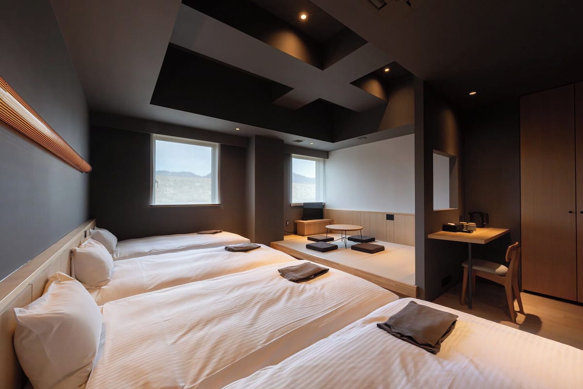 A modern hotel room with two beds, a desk, and a chair.
