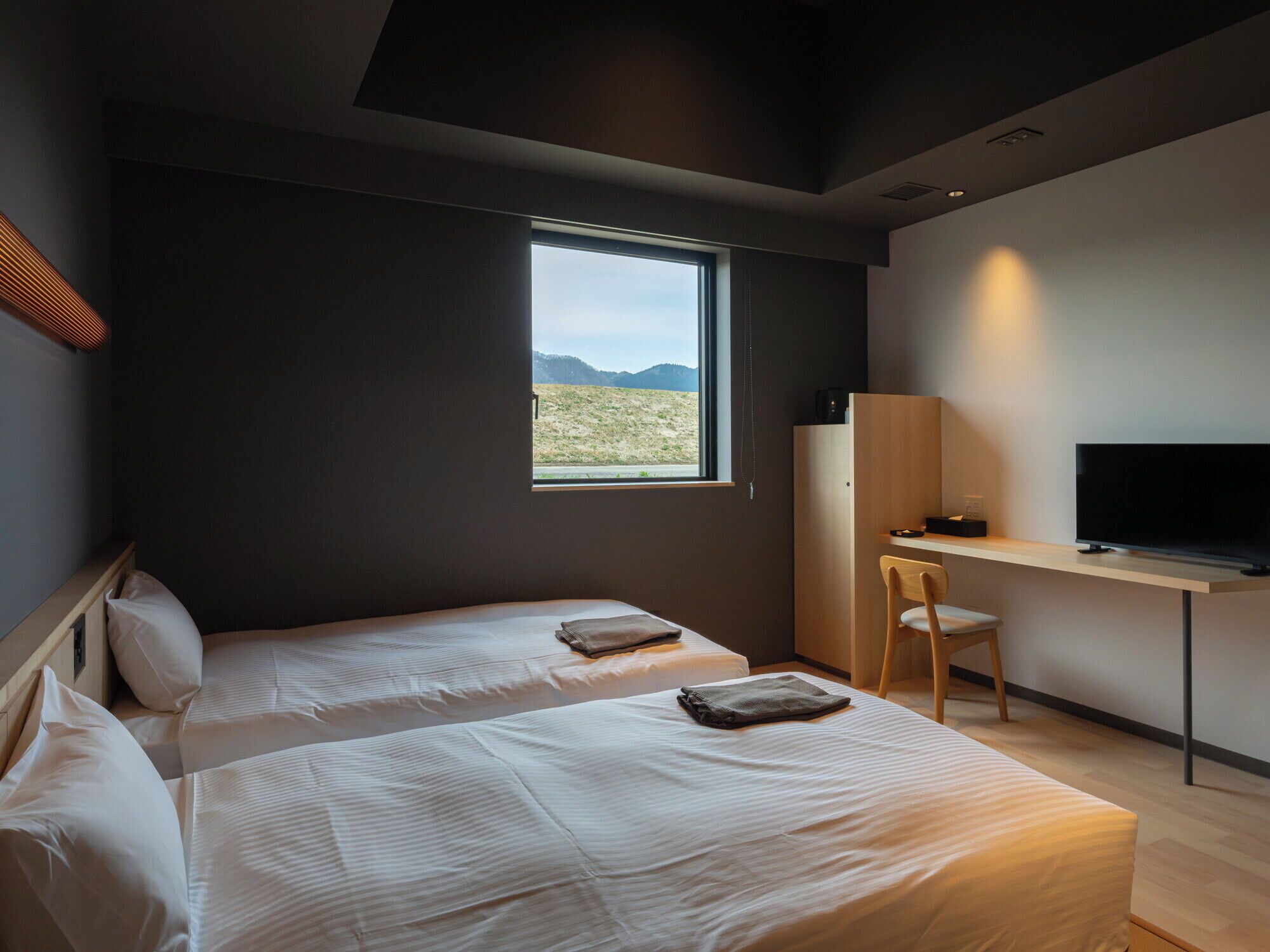 A modern hotel room with two beds, a desk, a chair, and a TV.
