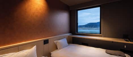 A hotel room with two beds, a large window with a view of the sea, and a built-in shelf above the beds.