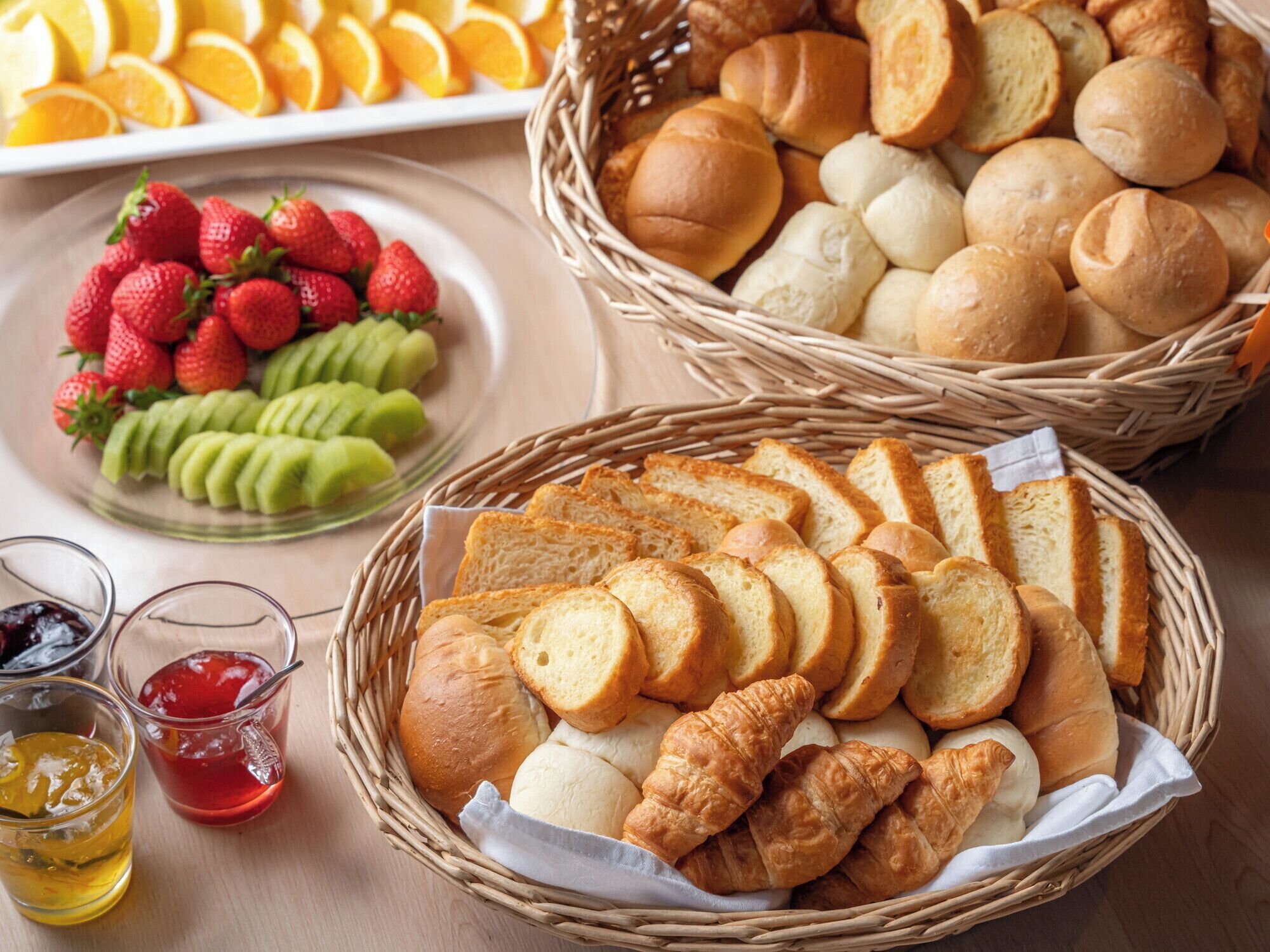 A table with baskets of bread, sliced bread, and fruit.