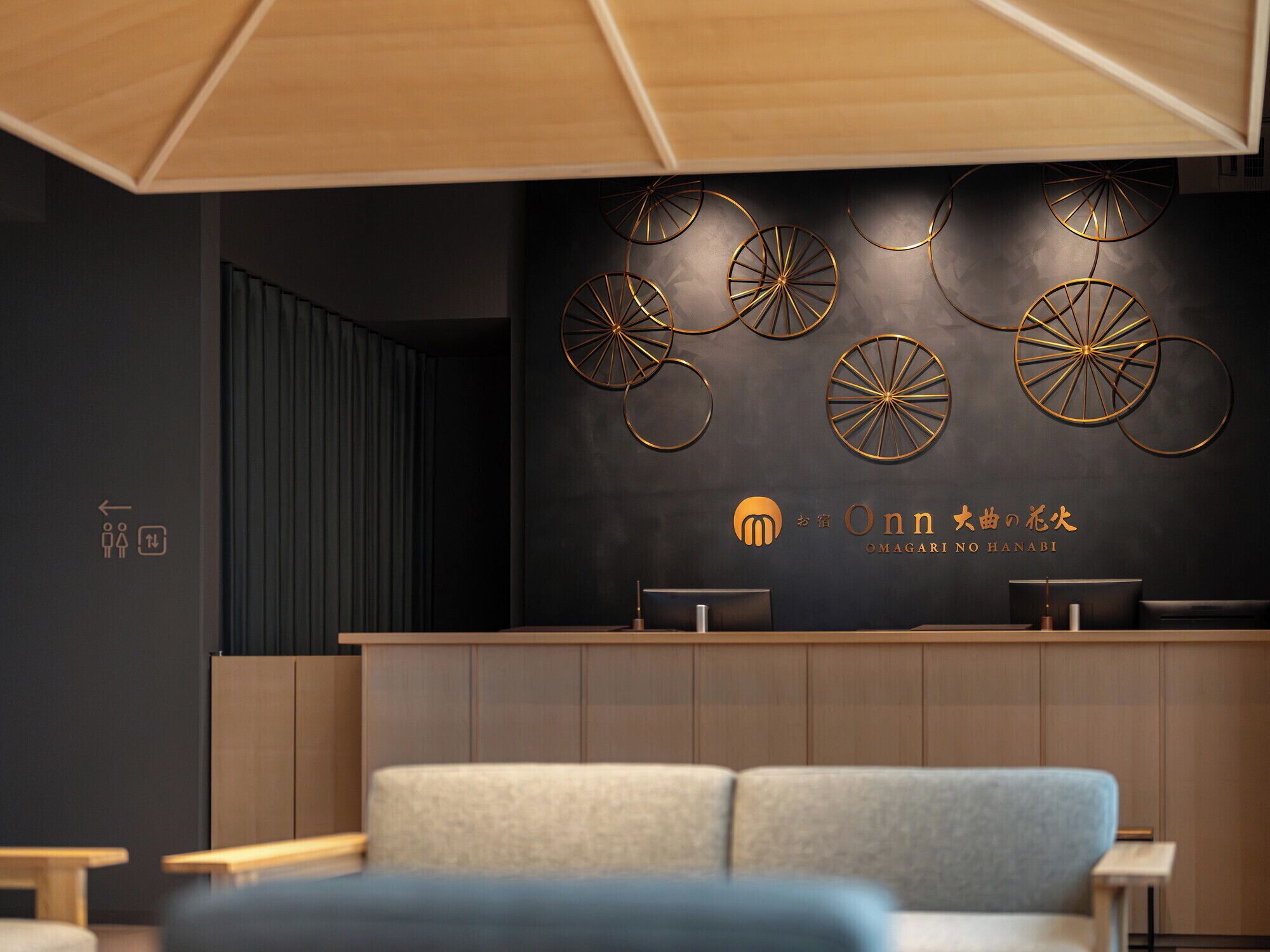 Un espace d’accueil moderne avec un mur foncé, un comptoir de réception et un coin salon agrémenté d’un canapé bleu.