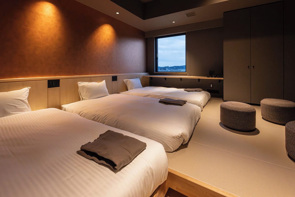 A hotel room with two beds, a large window, and a wardrobe.