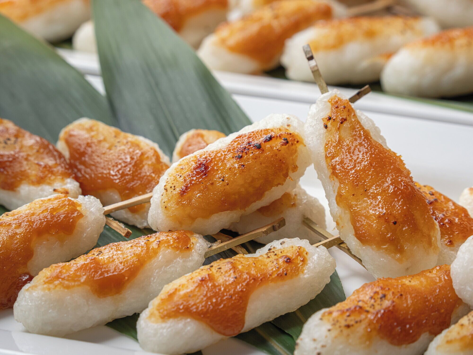 A plate of skewered food items, likely a type of grilled or roasted dish, served on a white plate with a green leaf garnish.