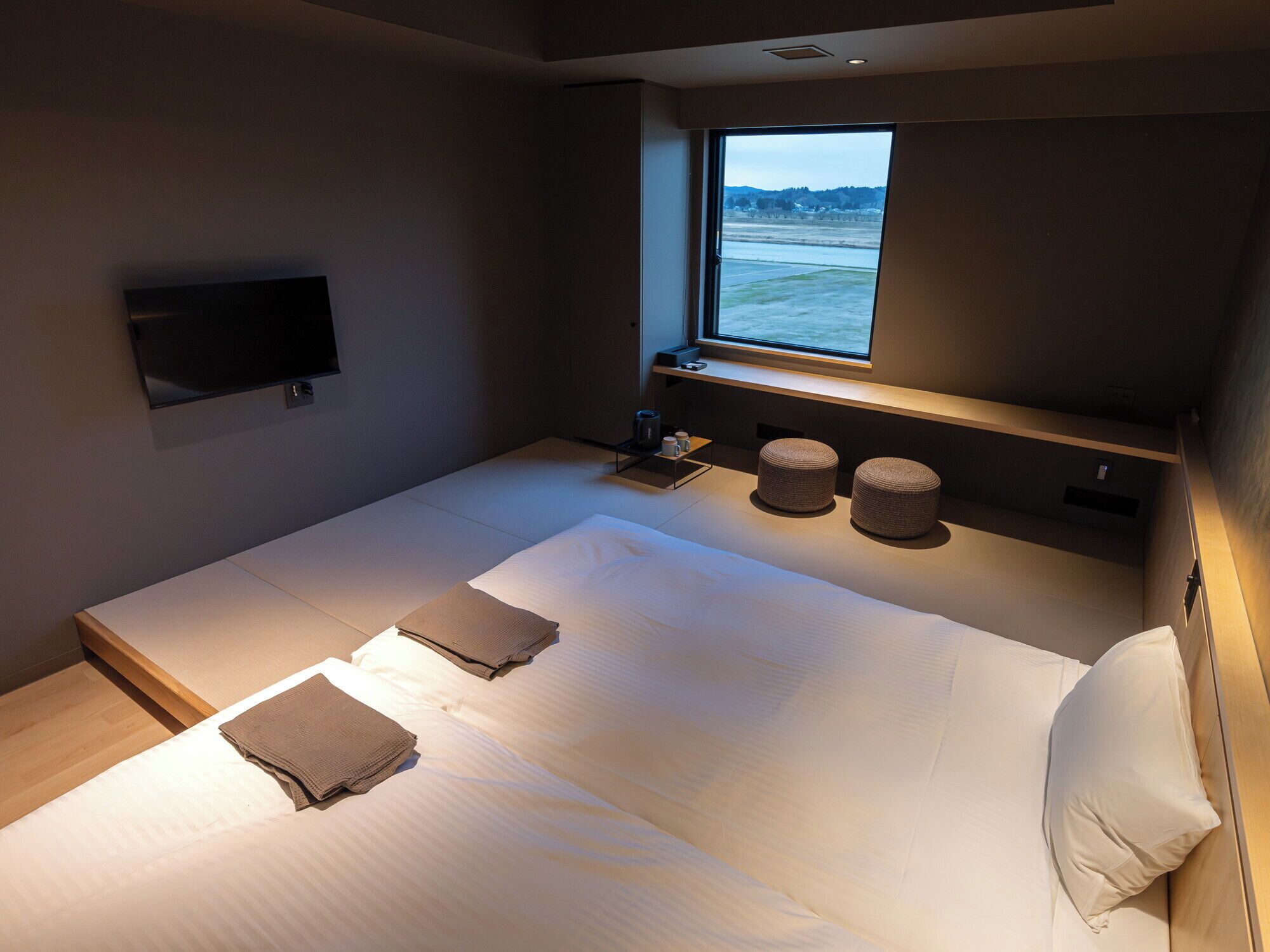 Una habitación de hotel moderna con una cama grande, un televisor instalado en la pared y un ventanal con vistas a un cuerpo de agua.