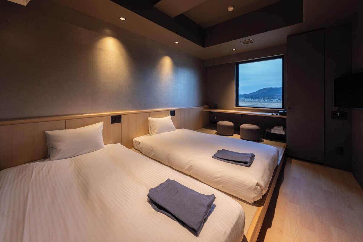 A modern hotel room with two beds, a large window with a view, and a flat-screen TV.