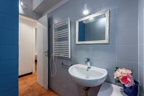 A bathroom with a white sink, a mirror with an ornate frame, a towel rack, and a vase with flowers.