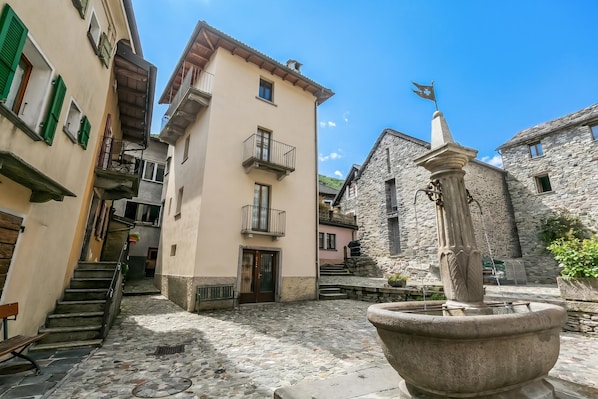 A cobblestone courtyard with a fountain, stone buildings, and a staircase.