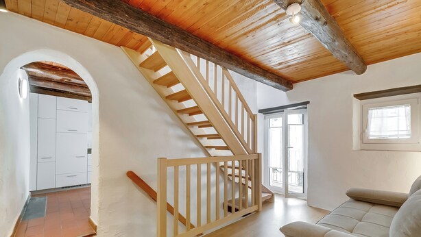 A staircase with wooden railings leading to a landing, a beige sofa, and a white door. - Ca dal 1785 Centovalli With Balcony and Parking (Centovalli)