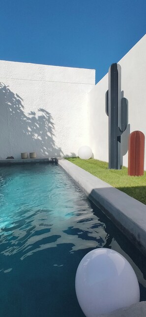 En swimmingpool med krystalklart, blåt vand, omgivet af en hvid mur og en græsplæne.