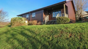 A two-story wooden house with a front porch, a small front yard, and a clear blue sky. - Creag Mhor Lodge (Arisaig)