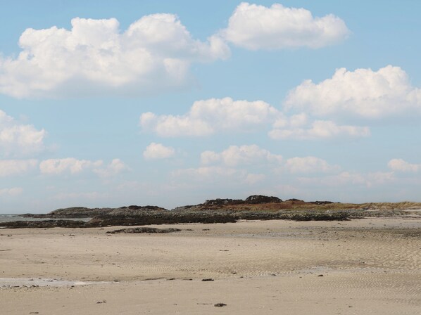 Una playa arenosa con afloramientos rocosos a lo lejos, bajo un cielo despejado.