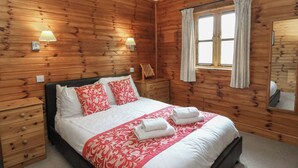 A wooden-paneled room with a bed, two bedside tables, and two wall-mounted lamps. - Creag Mhor Lodge (Arisaig)