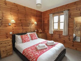Una habitación con paneles de madera, una cama, dos mesitas de noche y dos lámparas de pared.