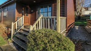 A wooden cabin with a porch, a wooden staircase, and a small garden area. - Creag Mhor Lodge (Arisaig)