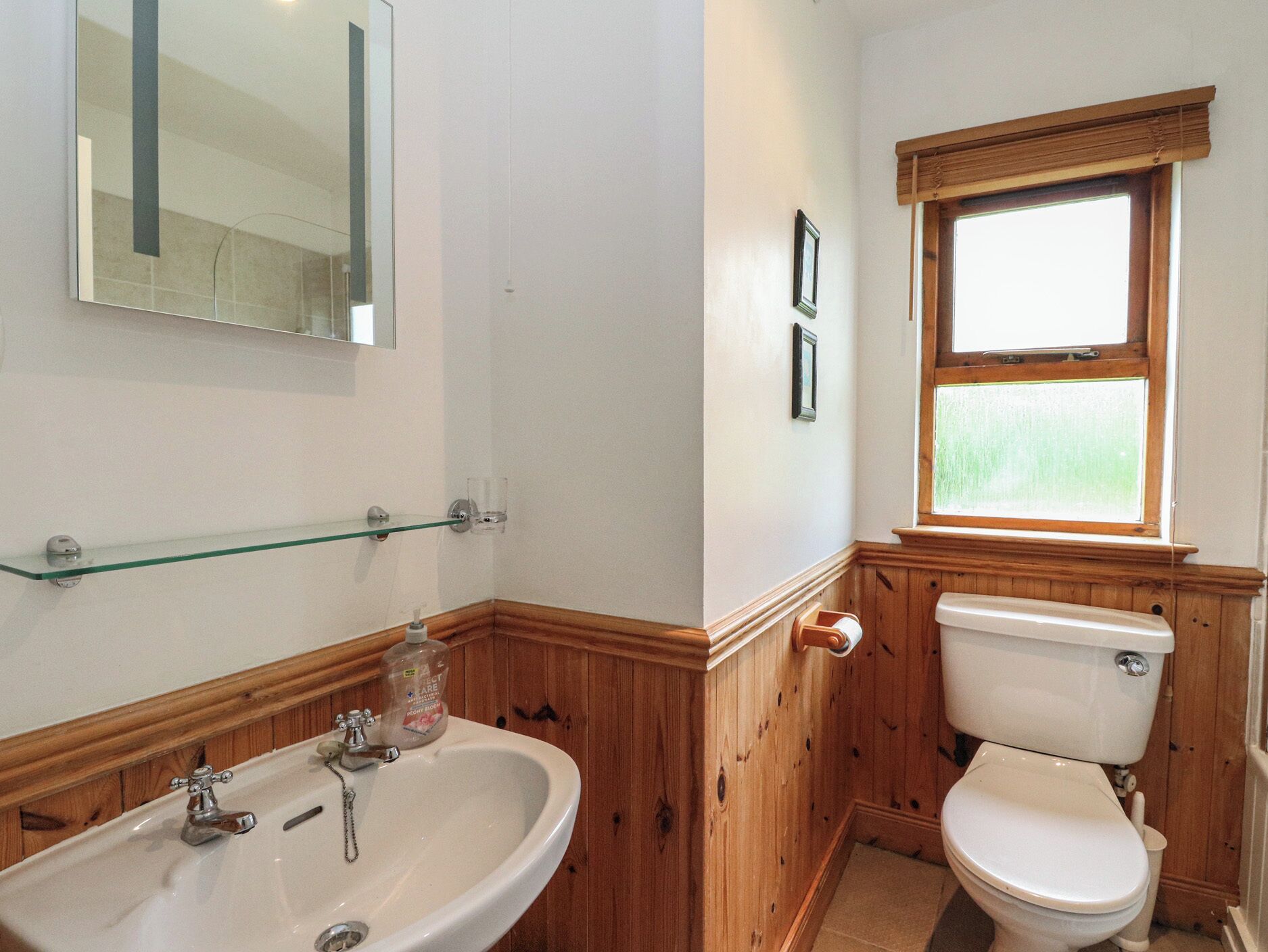 A bathroom with a wooden vanity, a sink, a toilet, and a window.