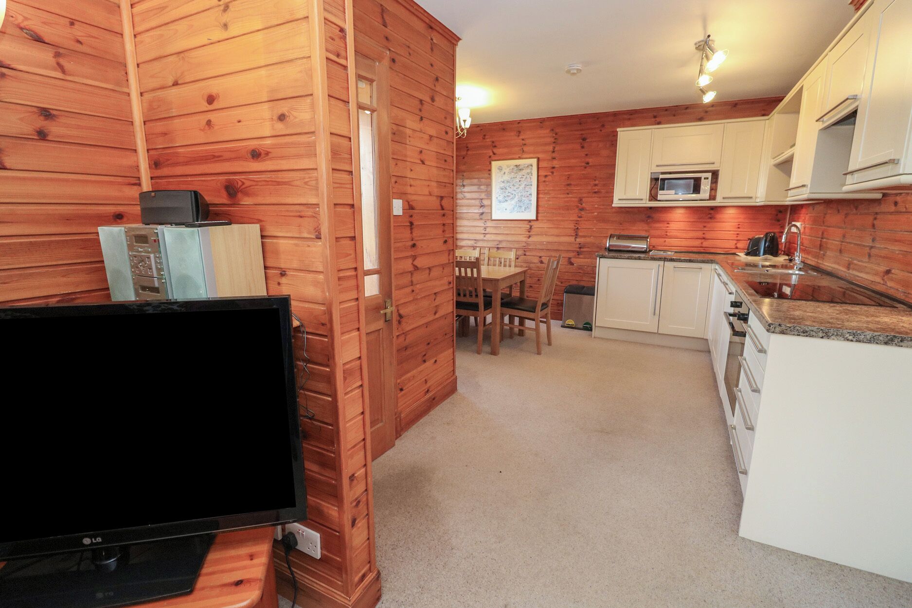 Una cocina compacta con paredes de madera, una zona de comedor y un televisor sobre un mueble.