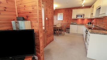 Una cocina compacta con paredes de madera, una zona de comedor y un televisor sobre un mueble.