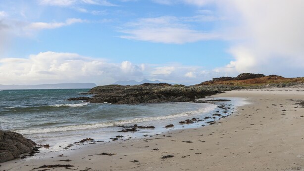 A beach with rocky outcrops, calm sea, and distant mountains. - Creag Mhor Lodge (Arisaig)