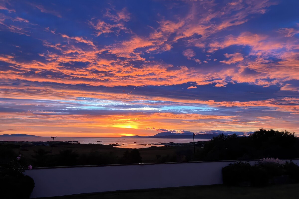Um pôr do sol sobre uma paisagem costeira com céu claro e montanhas ao longe.