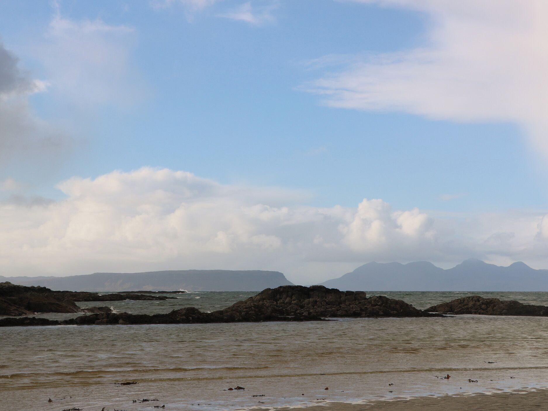 A coastal landscape with rocky outcrops and calm sea under a partly cloudy sky.