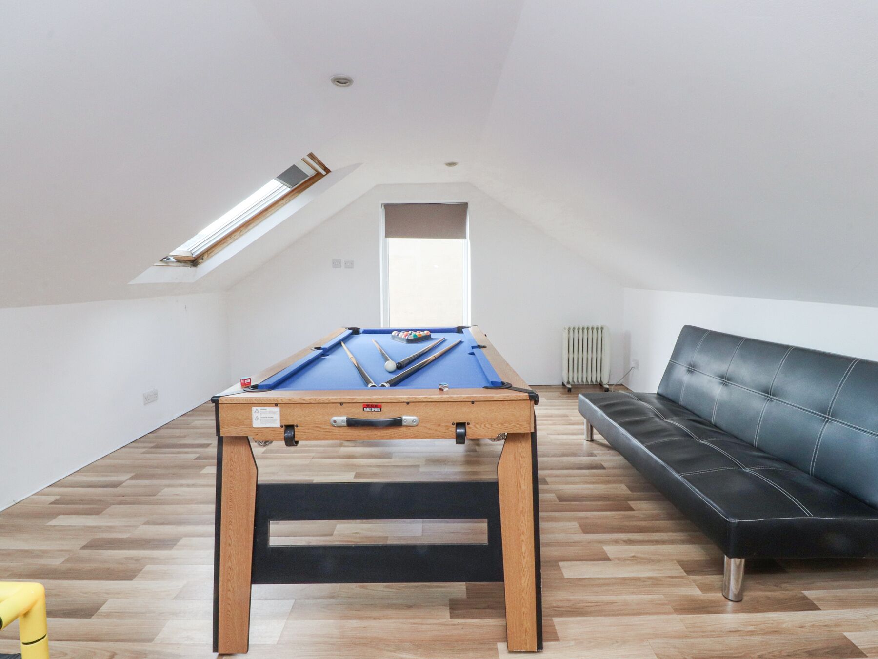 A room with a pool table, a black leather sofa, and a wooden floor.
