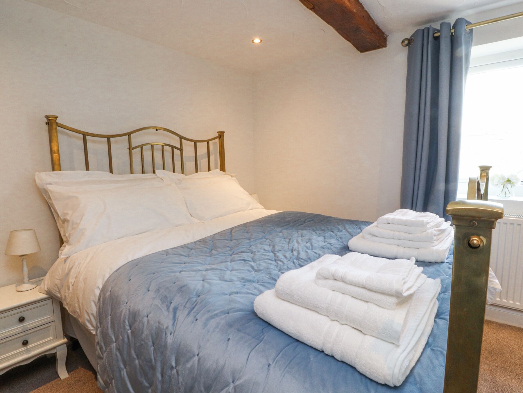 Un lit bien fait, avec une couette bleue, des oreillers blancs et une pile de serviettes pliées sur le côté.