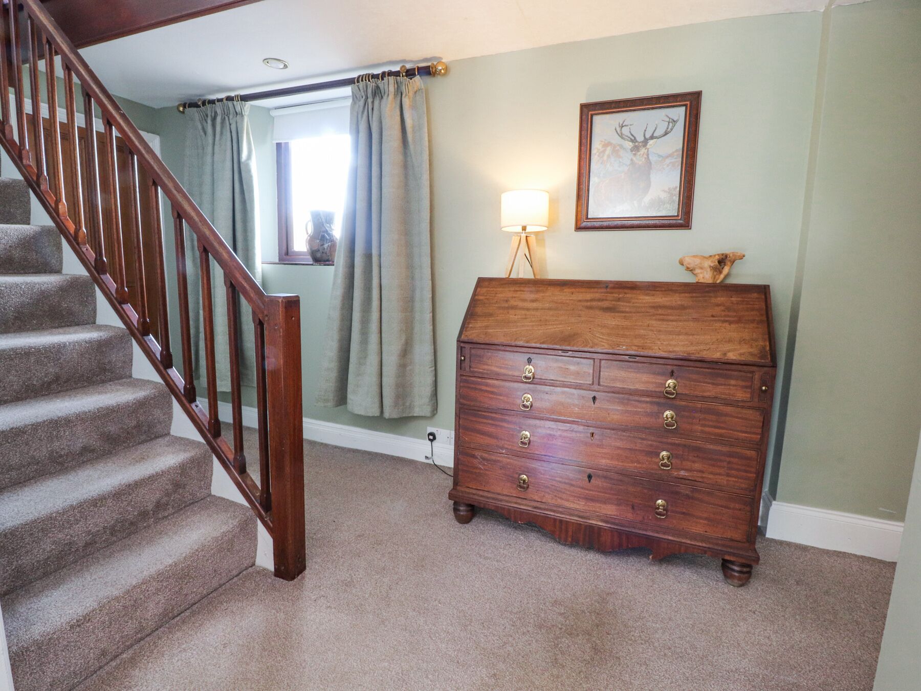 A staircase with wooden railings, a wooden dresser with drawers, a lamp, and a framed picture on the wall.